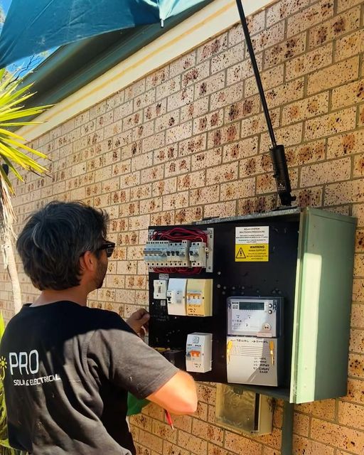 A Man Is Working On An Electrical Box On A Brick Wall — PRO Solar & Electrical In Lake Macquarie, NSW