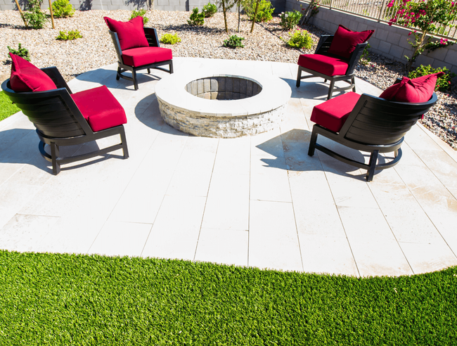Four black chairs with red cushions around a circular fire pit on a white patio by green grass.
