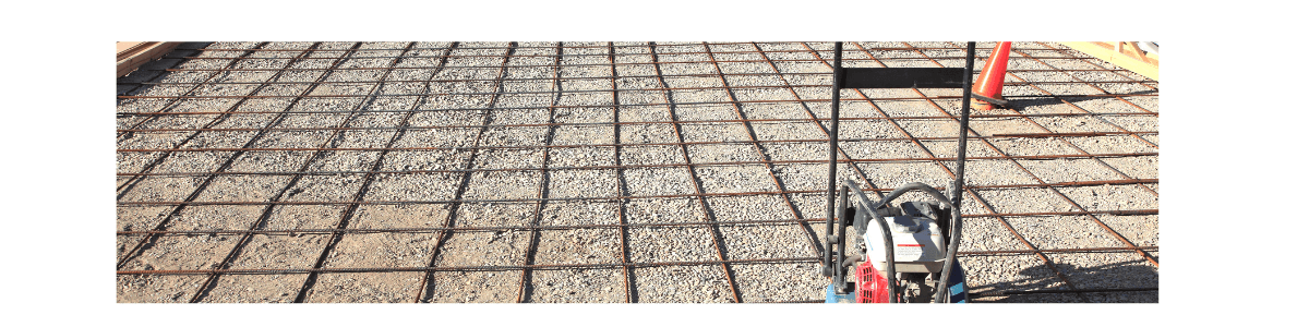 Construction site with rebar grid, tools, and a red cone on concrete ground