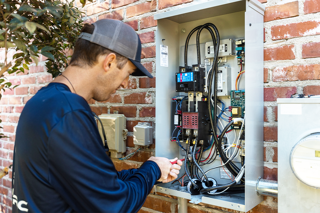 A man is working on an electrical box on a brick wall.