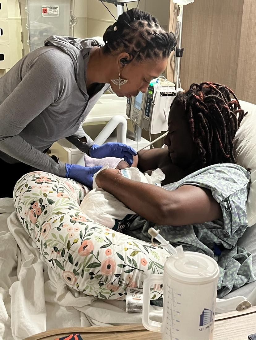 Woman in hospital bed holds newborn, another woman leans in to see baby.