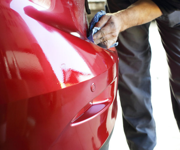 Person polishing a red car with a cloth
