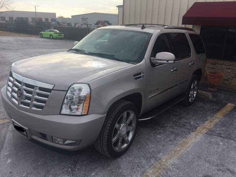 Silver Cadillac Escalade parked beside a building in a parking lot at dusk