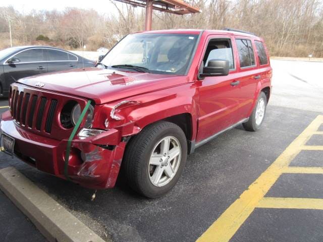 Damaged red SUV with front-end crash damage, parked in a lot near yellow curb markings