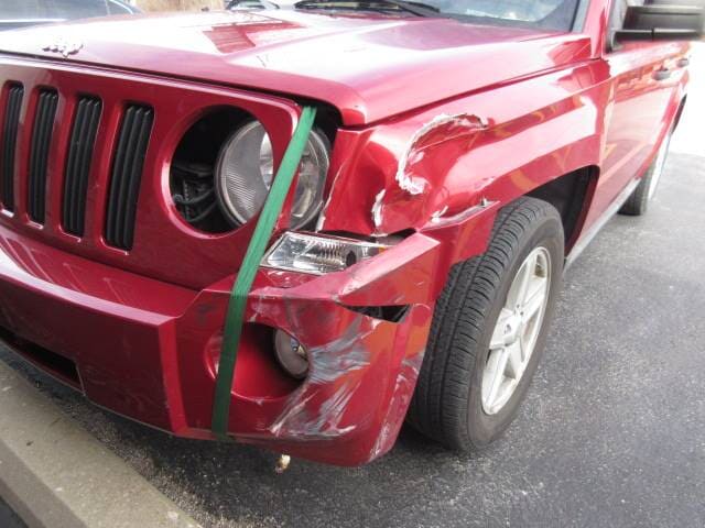 Red SUV with front-left fender and bumper smashed, showing a damaged headlight after a crash