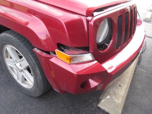 Red SUV front bumper damaged, with dented fender and broken trim near the wheel.