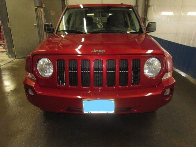 Front view of a red Jeep SUV parked indoors with a blue-covered license plate.