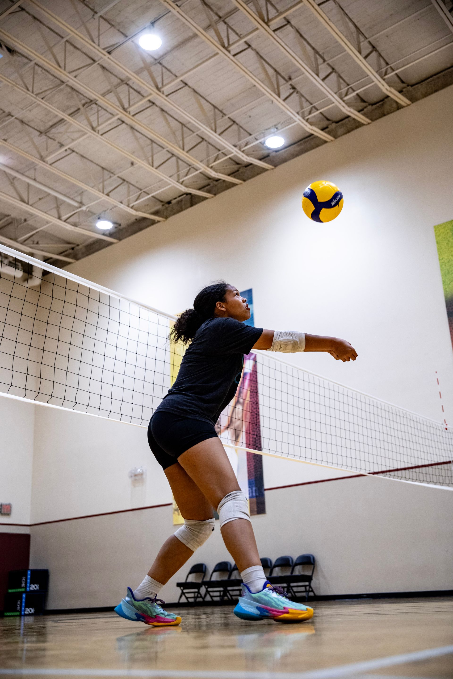 Indoor volleyball player in dark uniform sets a yellow-and-blue ball near the net