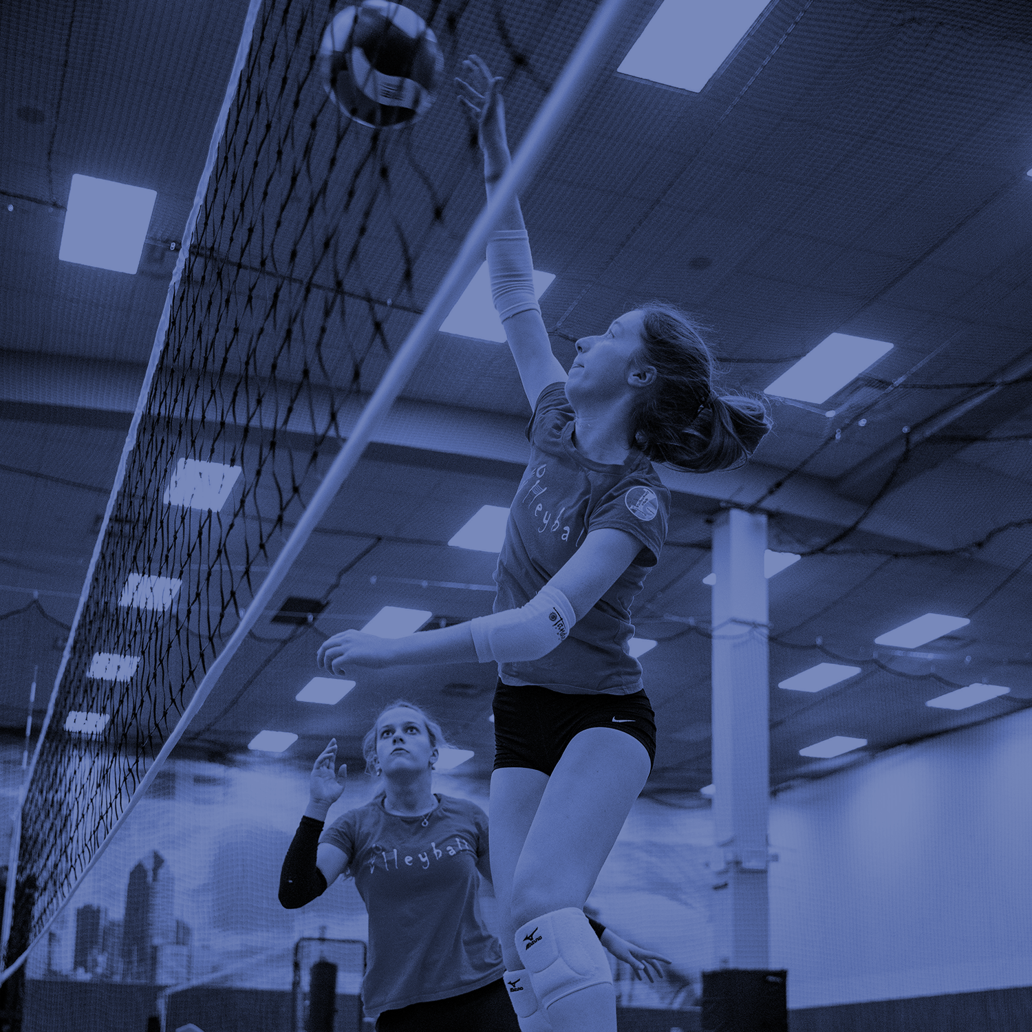 Indoor volleyball players jumping at the net for a spike during a match
