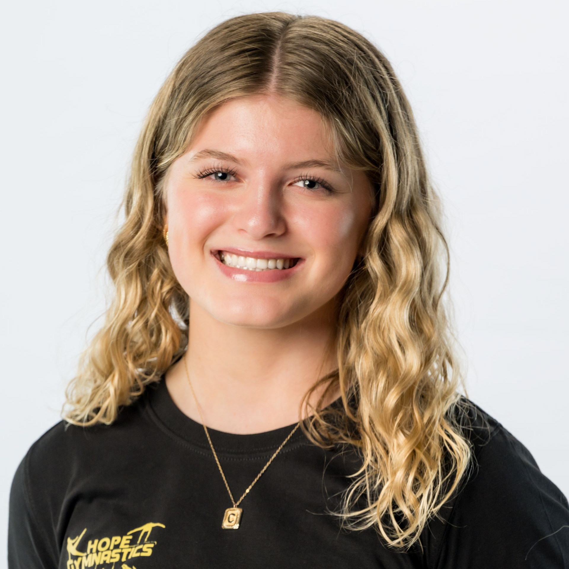 Portrait of a smiling person in a black T-shirt with a gold necklace on a light background
