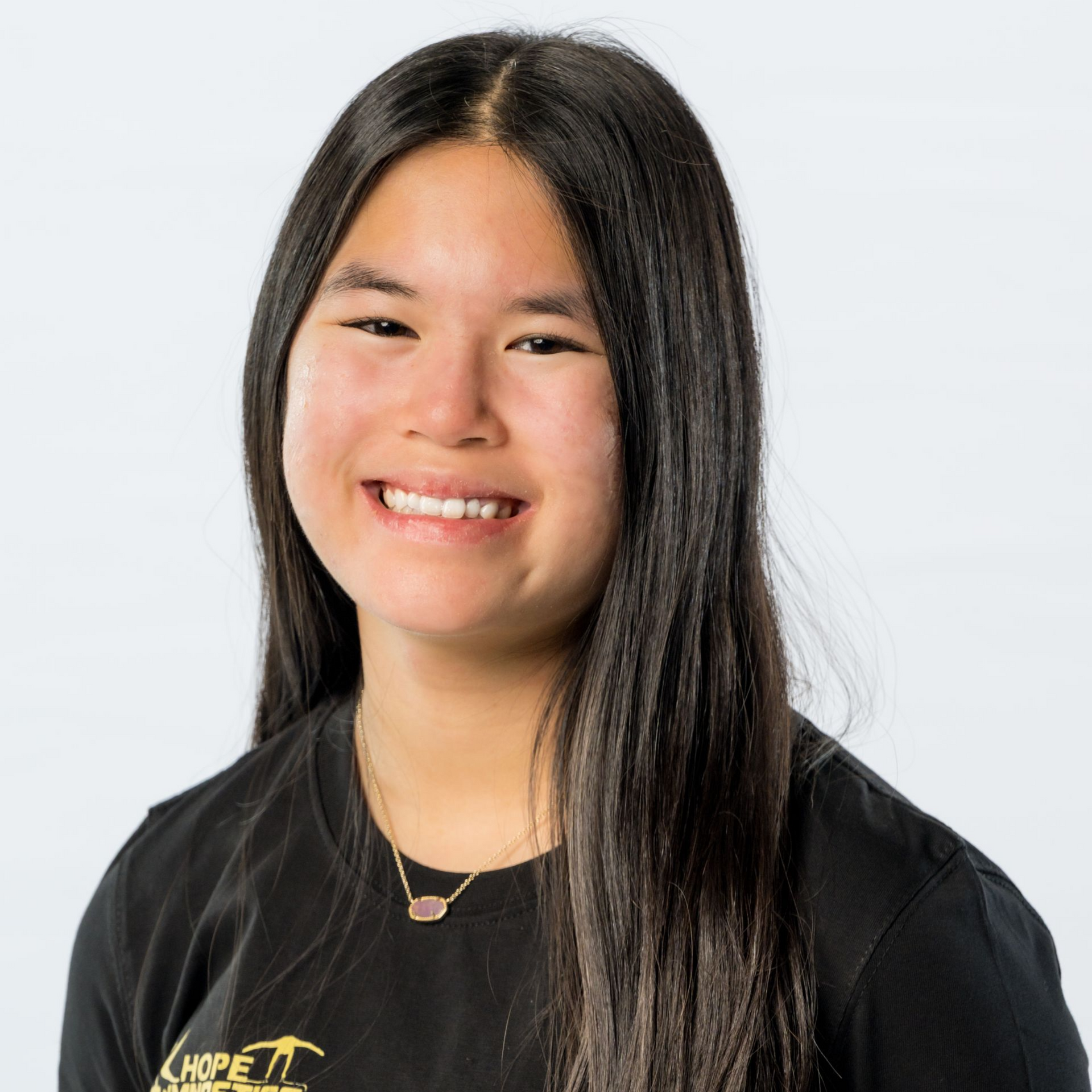 Smiling woman with long dark hair wearing a black shirt against a light background