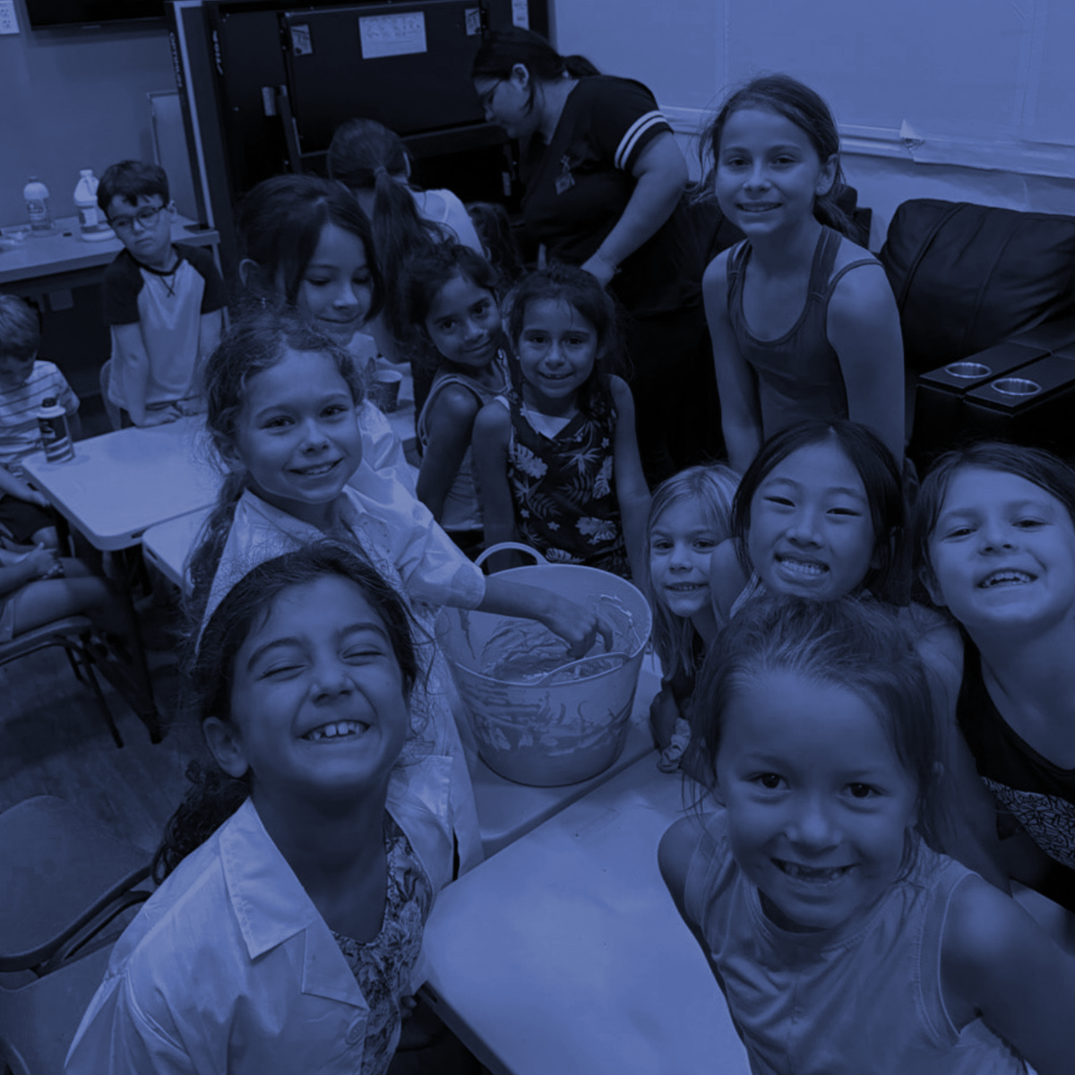 Smiling children gathered around a table indoors, posing for a group photo.