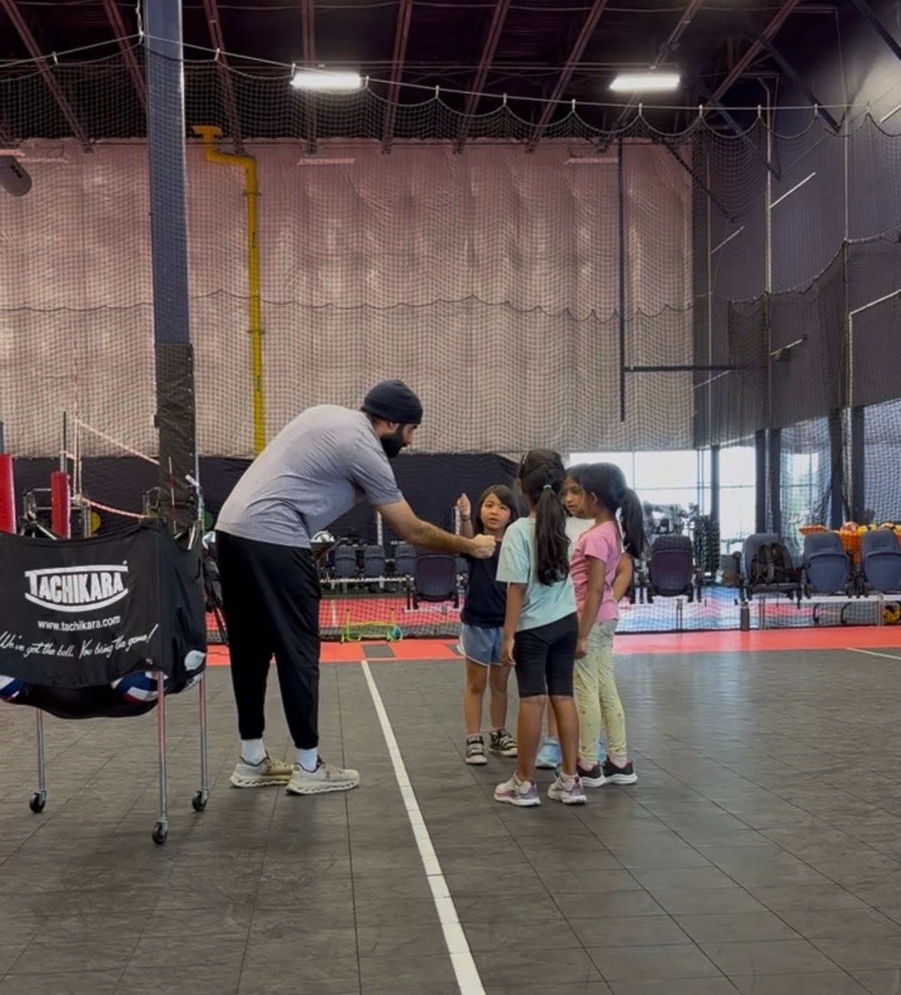 Coach speaking to three children on an indoor sports court.