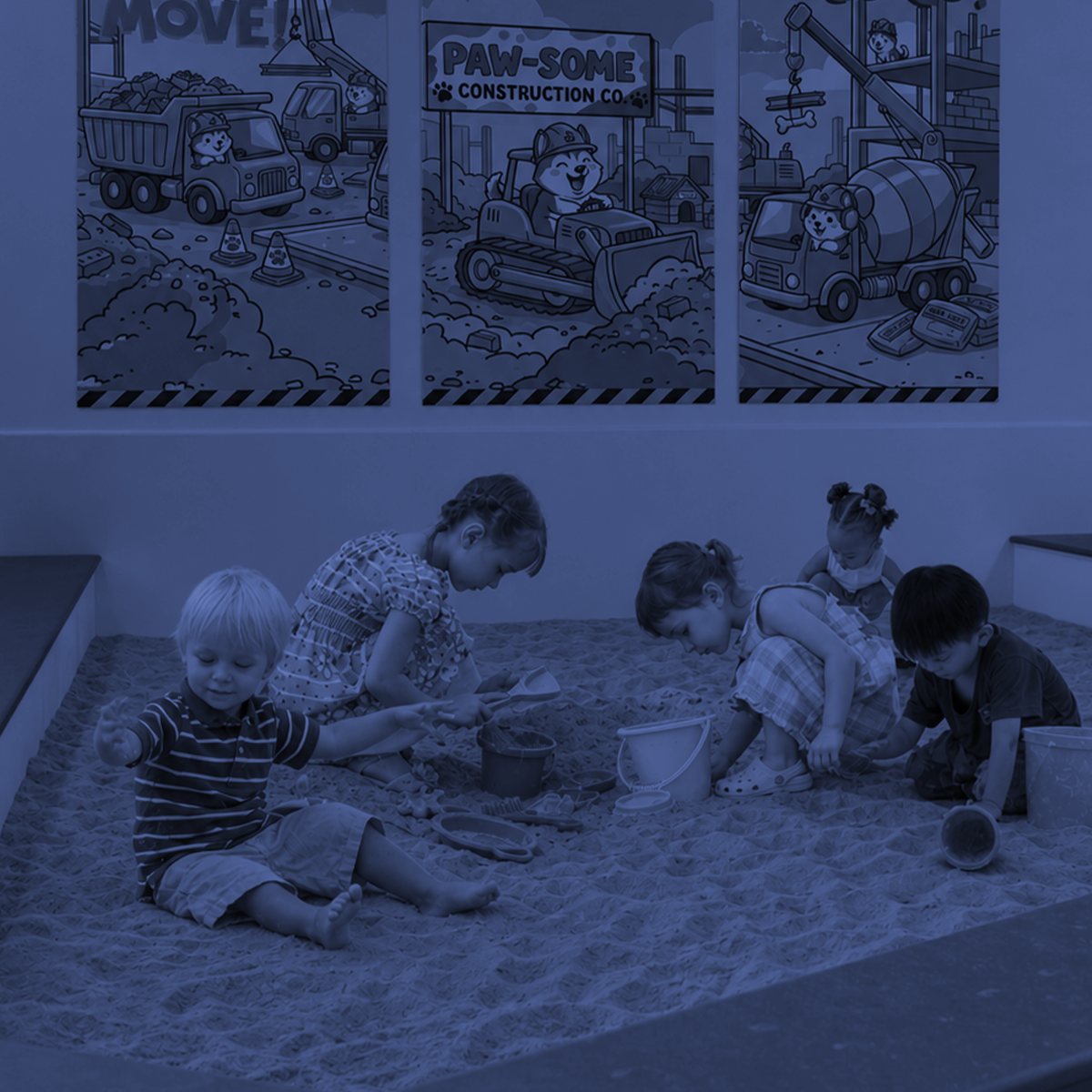 Children playing in a sandbox indoors under posters on the wall