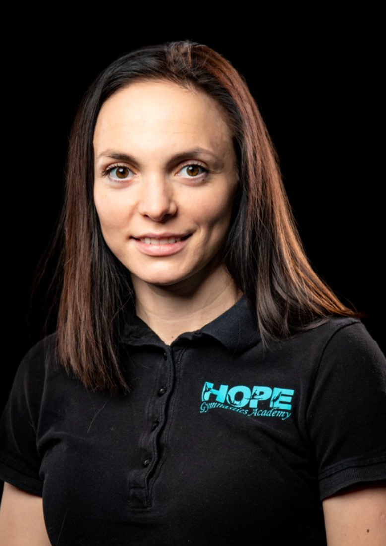 Woman in black polo shirt with turquoise “HOPE” logo, smiling against a dark background