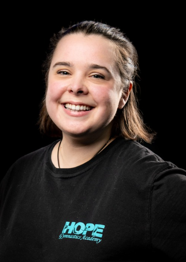 Smiling person in black shirt with blue logo against a dark background