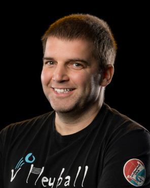 Smiling man in a black “Volleyball” T-shirt against a dark background