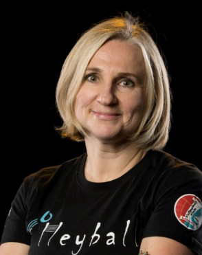 Smiling woman in a black Hevball shirt against a dark background