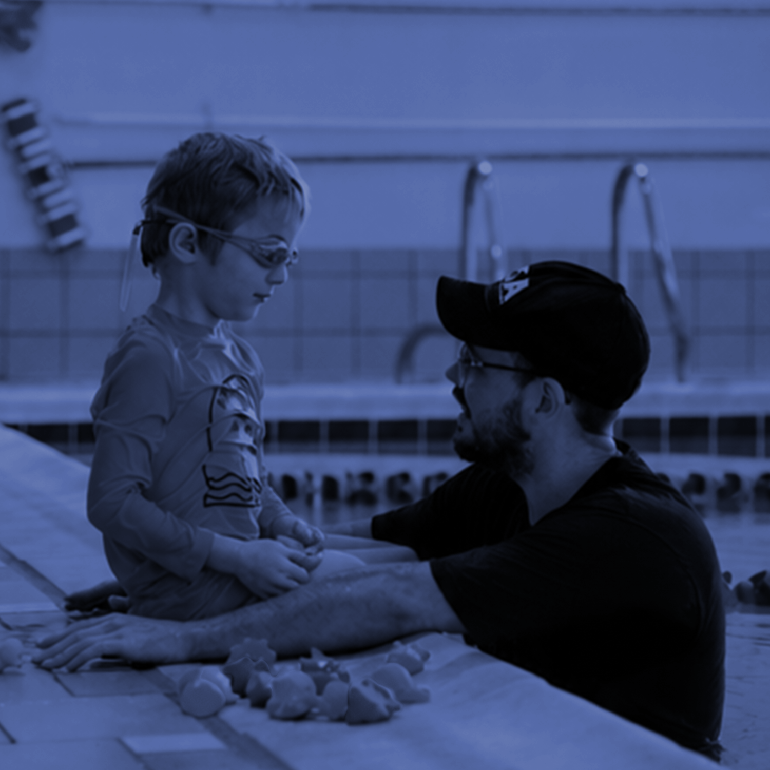 Adult and child talking at a poolside table, both reaching toward small blocks or toys under blue lighting