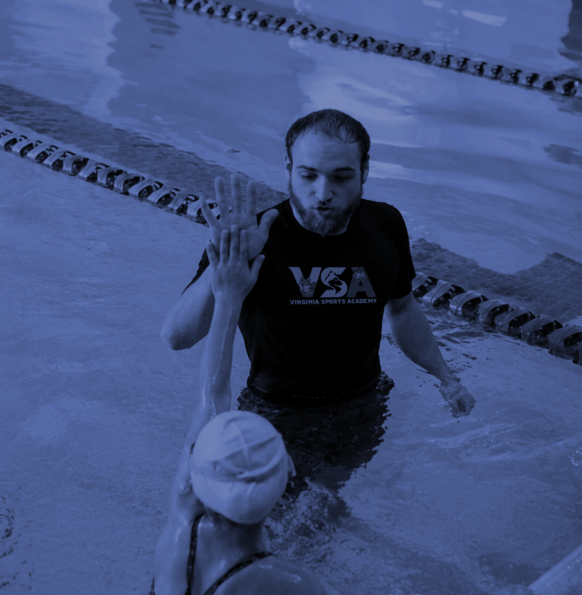 Swimmer in pool lifting hand to coach at edge of lane, both in blue-tinted water.