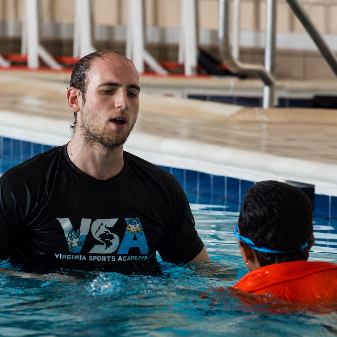 Swim instructor in black shirt coaching a swimmer in an indoor pool