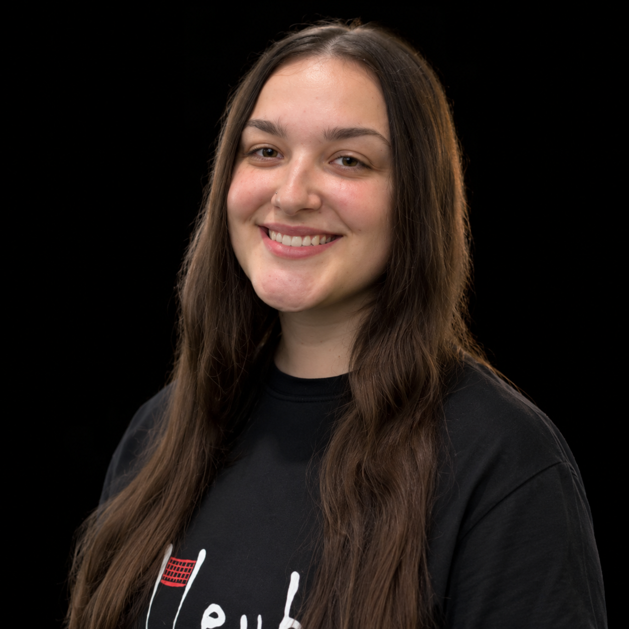 Smiling person with long dark hair wearing a black shirt against a black background