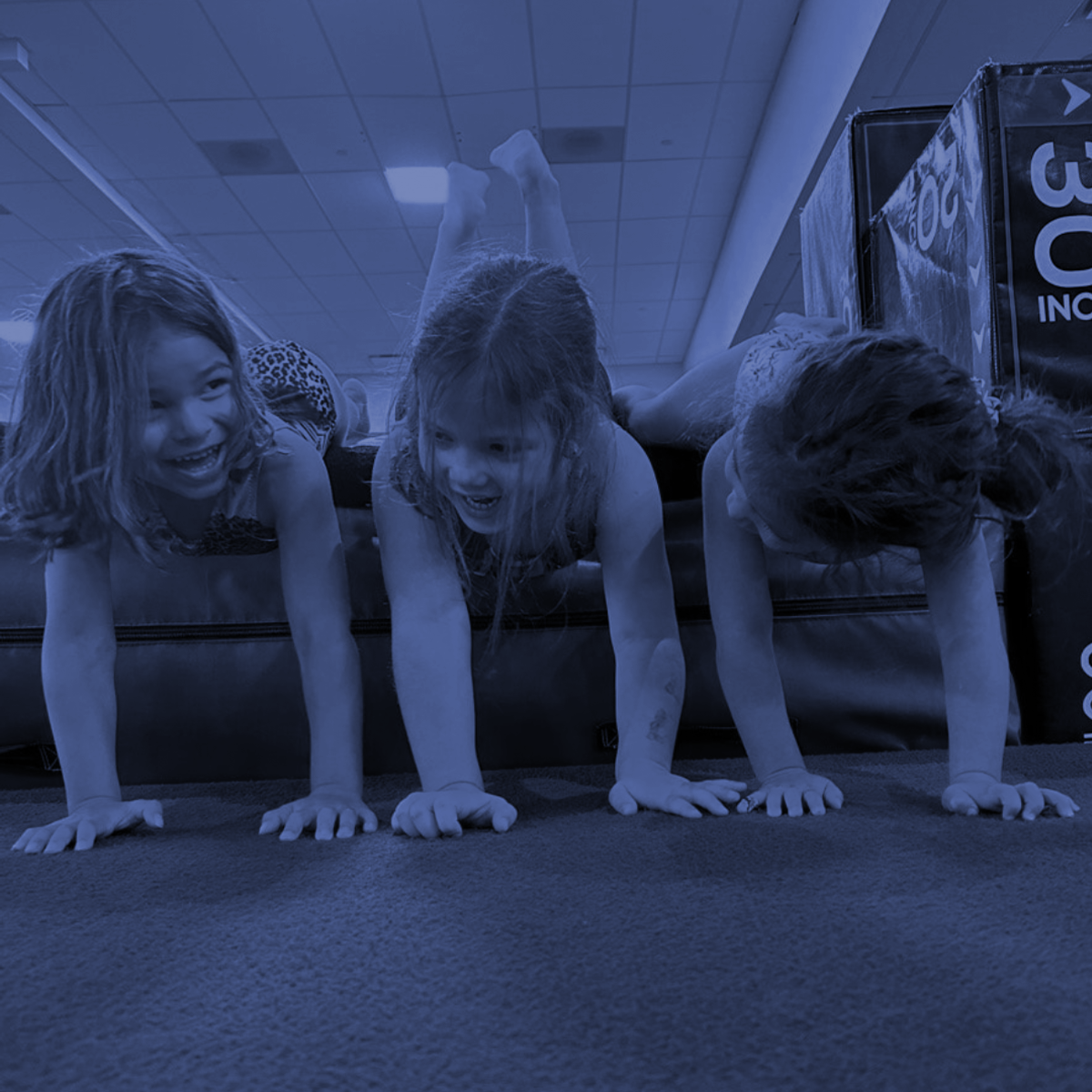 Children doing push-ups on a gym floor under blue lighting, smiling and laughing.