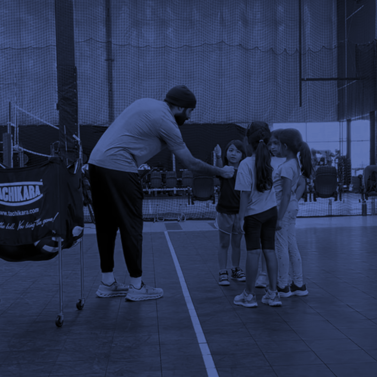 Coach speaking to a small group of children on an indoor basketball court, tinted blue.