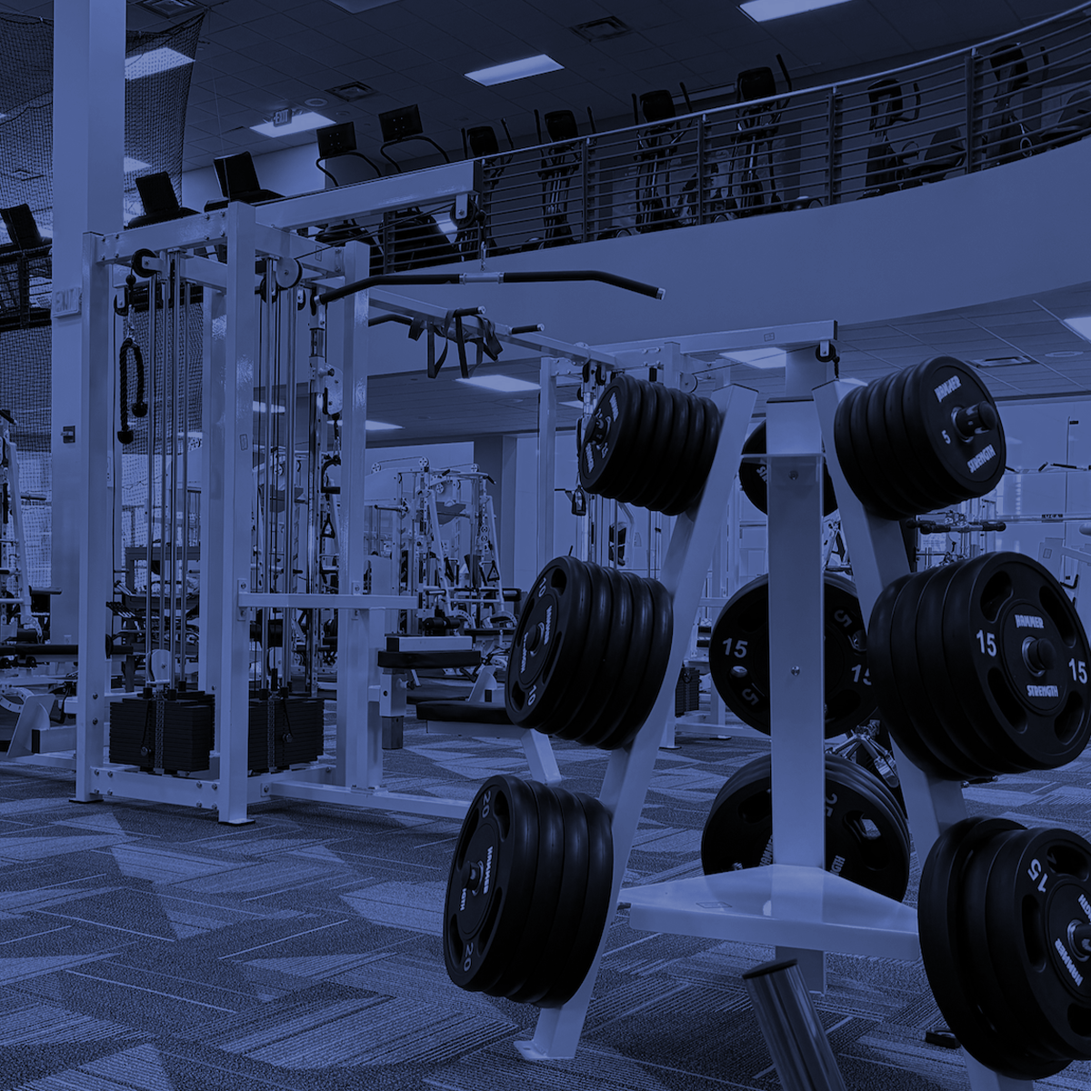 Weight room with gym machines and racks of weight plates under blue lighting
