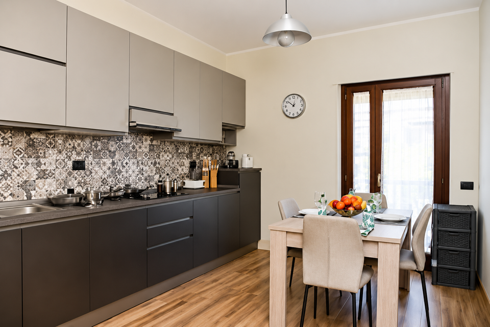 Cucina moderna con mobili scuri, paraschizzi decorato e tavolo da pranzo vicino alla finestra.