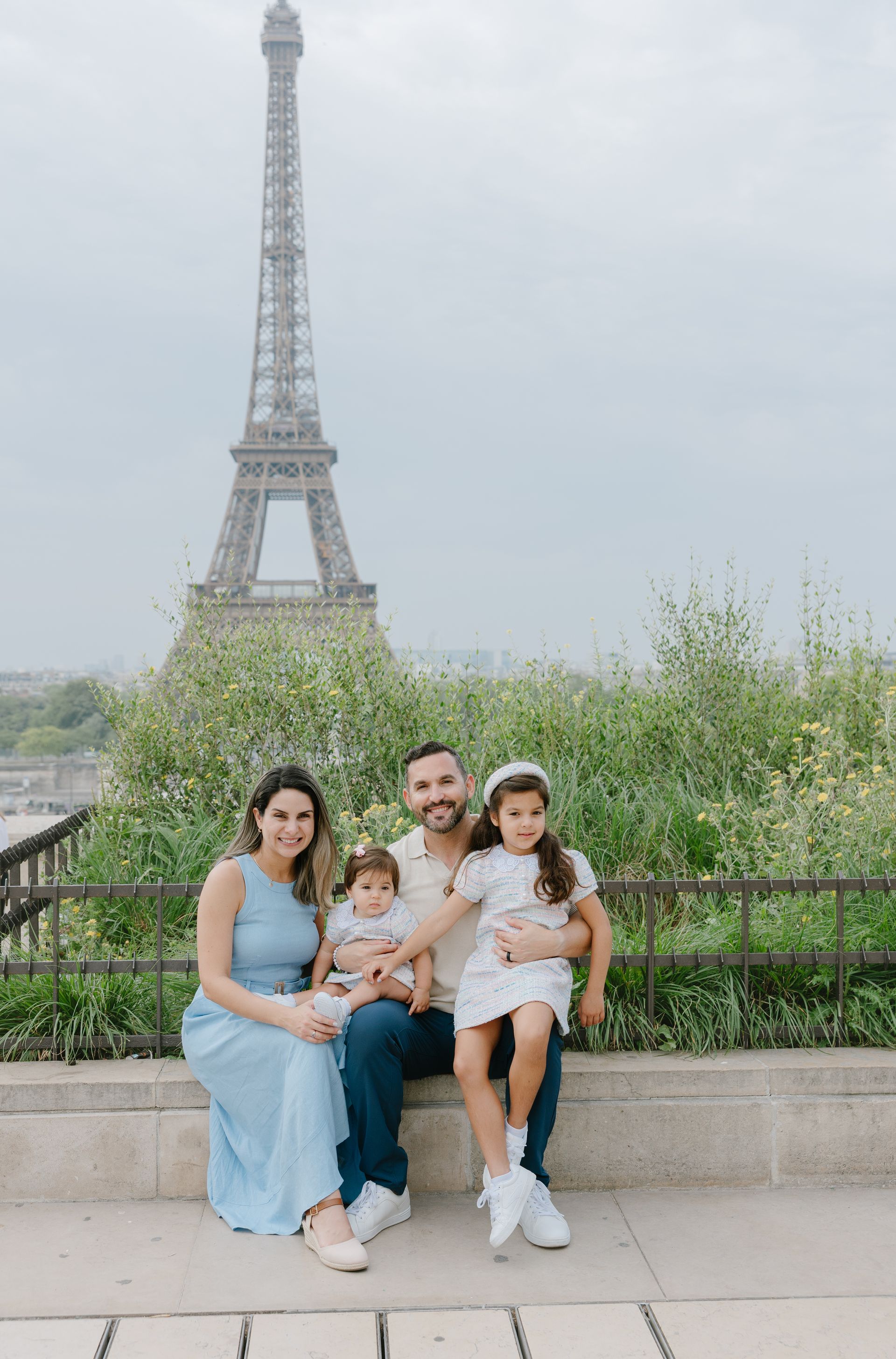 Family seated in front of the Eiffel Tower, with a cloudy sky and greenery in the background