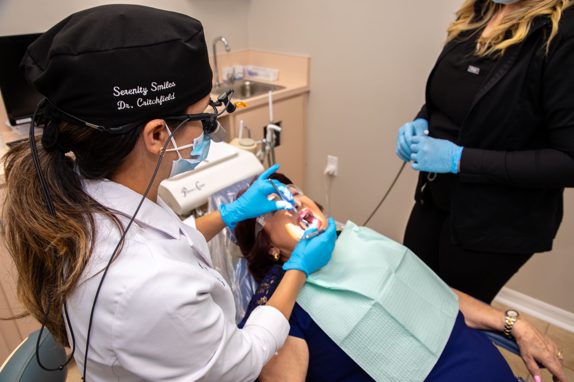 Dentist in white coat cleaning a patient’s teeth with blue-gloved hands in a dental clinic