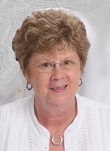 Portrait of a woman with short curly hair, glasses, and silver jewelry against a light gray background