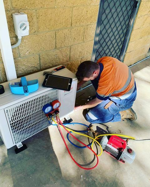 A Man Is Working on An Air Conditioner Outside of A Building — Paton's Electrical Services in Craignish, QLD