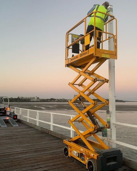 A Man Is Working on A Pole on A Scissor Lift — Paton's Electrical Services in Urangan, QLD