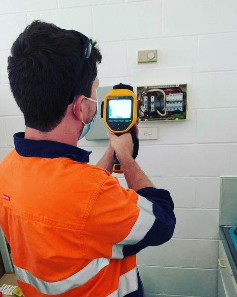 A Man in An Orange Shirt Is Holding a Yellow Device — Paton's Electrical Services in Urangan, QLD