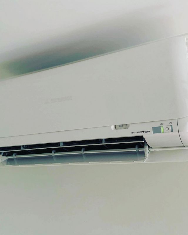 A White Air Conditioner Is Hanging on A White Wall — Paton's Electrical Services in Hervey Bay, QLD