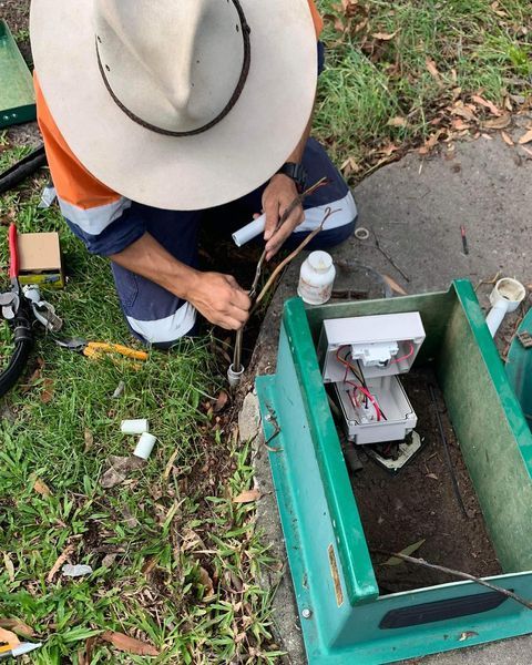 A Man Wearing a Hat Is Working on A Green Box — Paton's Electrical Services in Torquay, QLD