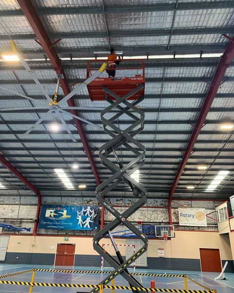 A Man Is Standing on A Scissor Lift in A Warehouse — Paton's Electrical Services in Urraween, QLD