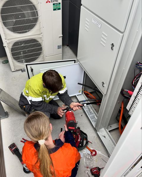 A Man and A Woman Are Working on An Electrical Box — Paton's Electrical Services in Urangan, QLD