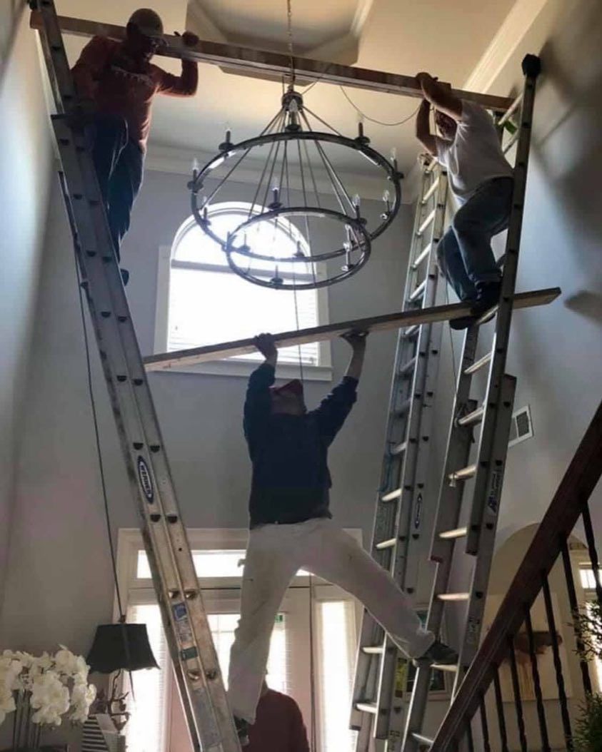 A Group of Men Are Working on A Chandelier in A Living Room — Paton's Electrical Services in Urangan, QLD