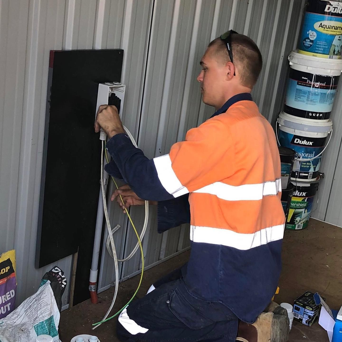 A Man in An Orange and White Striped Shirt Is Working on An Electrical Outlet — Paton's Electrical Services in Pialba, QLD