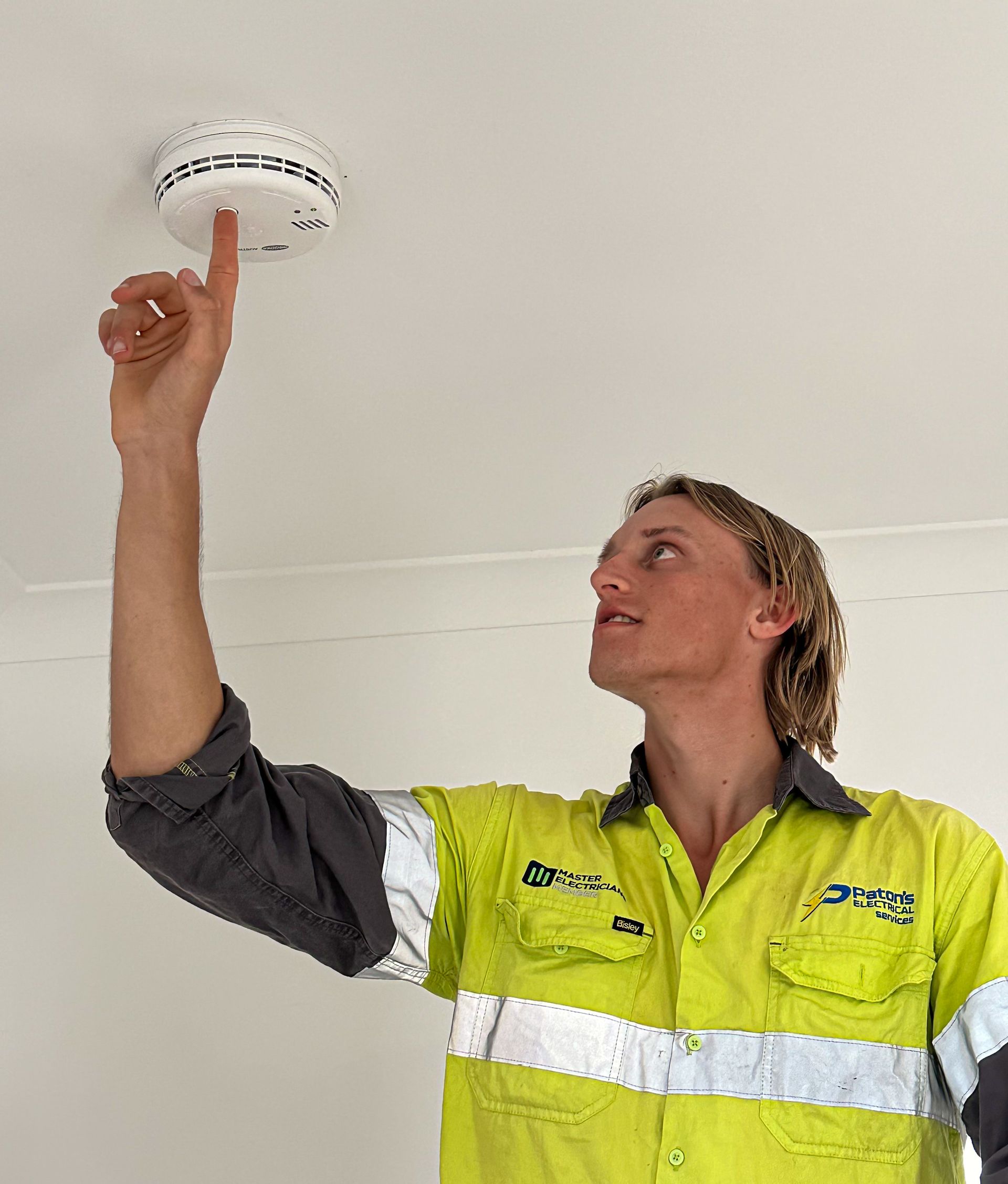 A Man Is Standing on A Ladder Working on A Ceiling — Paton's Electrical Services in Hervey Bay, QLD