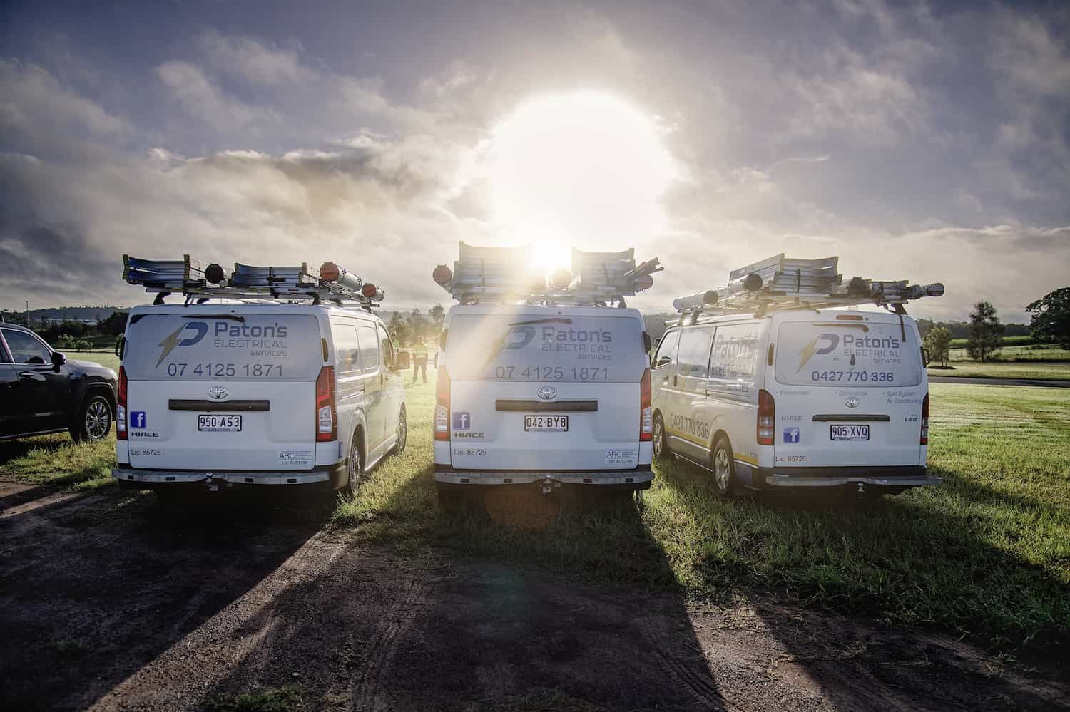 Three Vans Are Parked In A Field With The Sun Shining Through Them — Paton's Electrical Services in Craignish, QLD