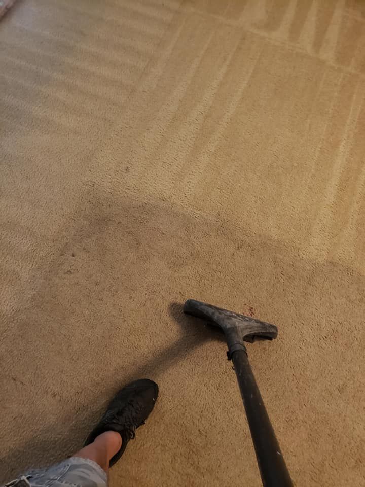A person uses a vacuum cleaner on a beige carpet, showing a clear contrast between the cleaned and uncleaned sections.
