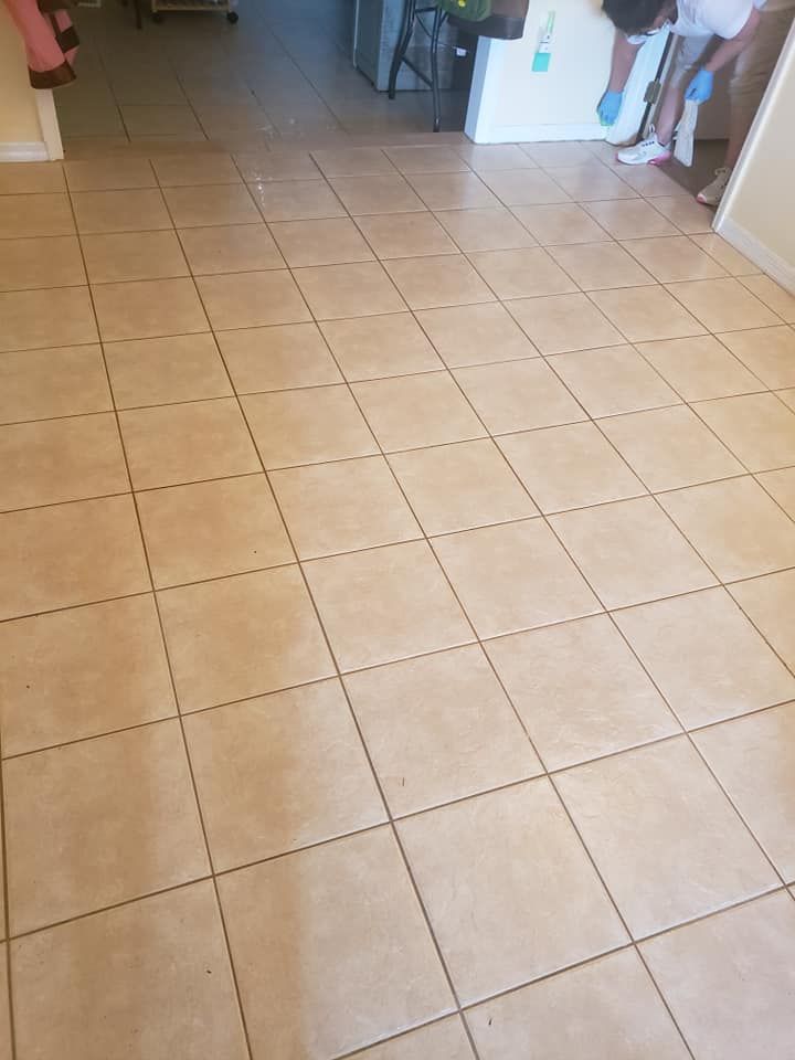 A person wearing blue gloves stands in a doorway, cleaning a beige tiled floor in a residential space.