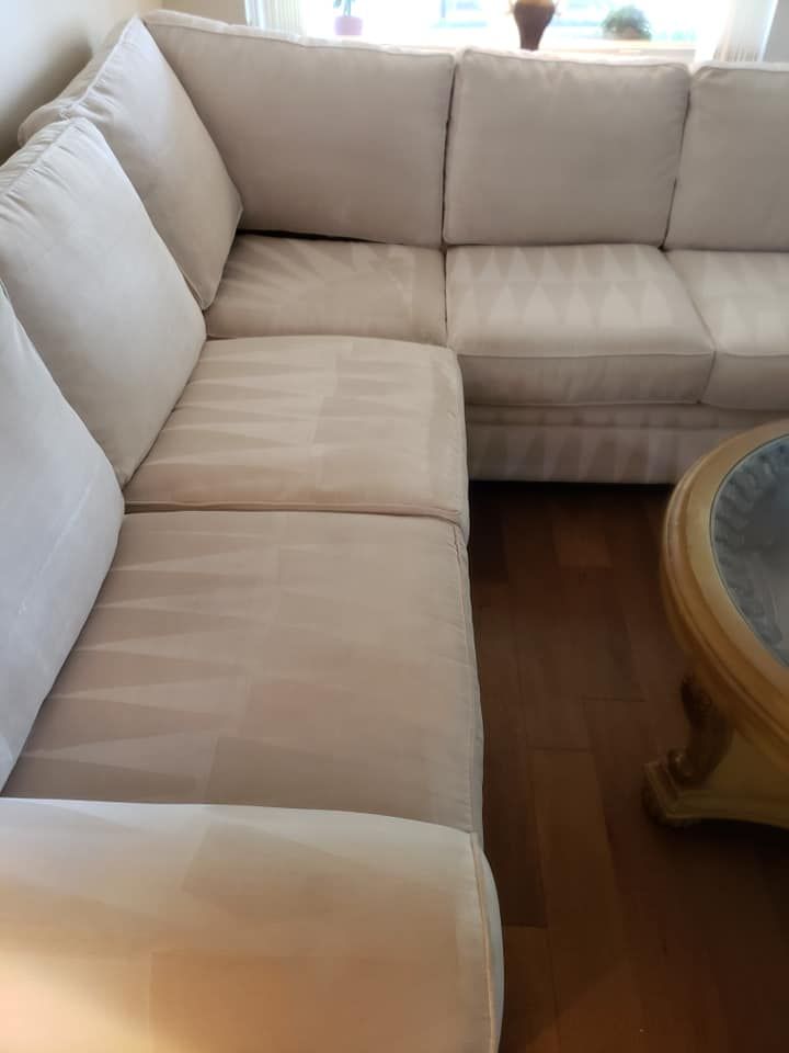 A cream-colored sectional sofa sits on a wooden floor in a brightly lit room next to a circular wooden coffee table.