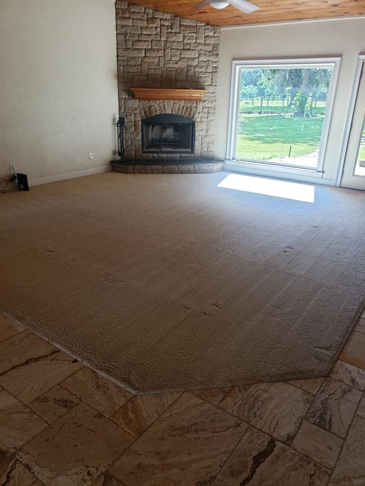 A spacious room with stone tile flooring transitioning into a large, beige-carpeted area facing a stone fireplace.