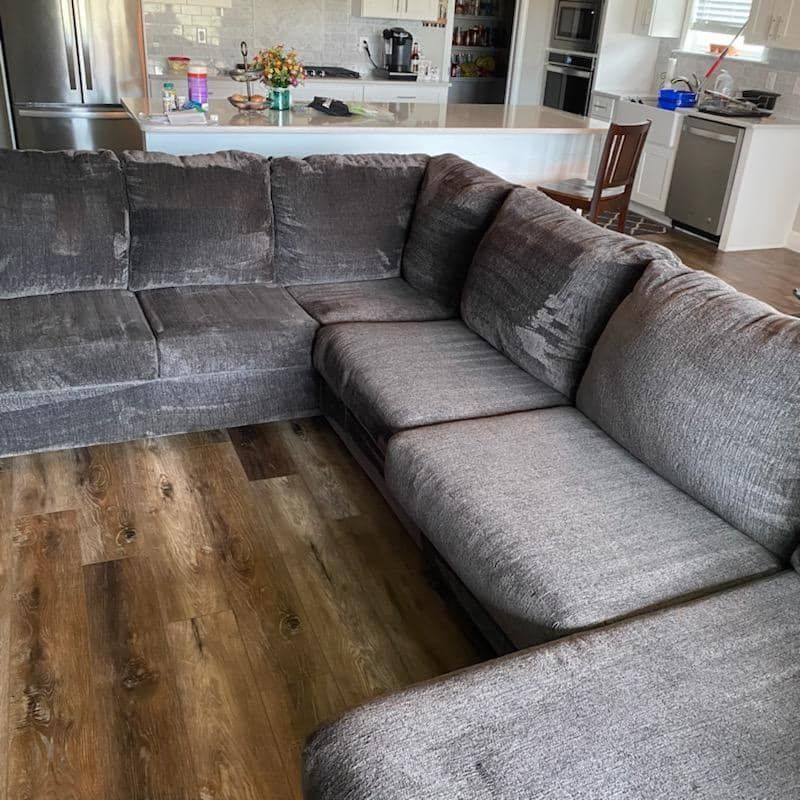 A grey sectional sofa sits on a wood floor in a brightly lit, open-concept kitchen space.