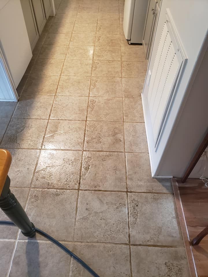 A long hallway with square, beige, textured floor tiles leading past a white wall with a louvered vent cover.